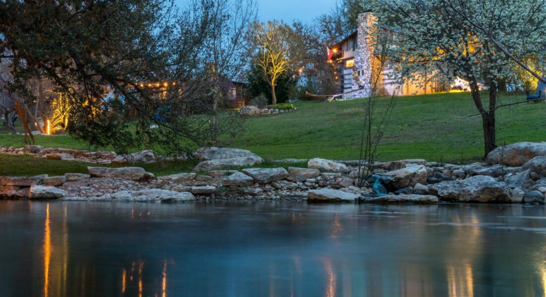 a serene view of a body of water with a rocky shoreline, trees, and a building in the background