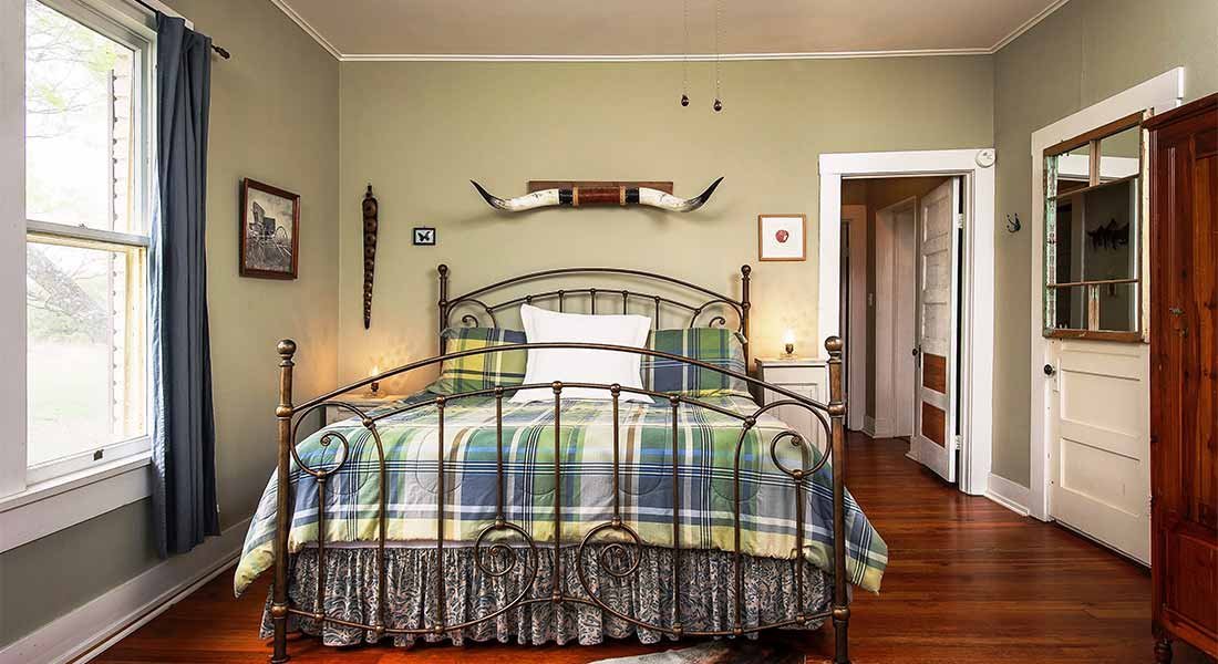 A wide view of a bedroom with a plaid bedspread and metal bed frame