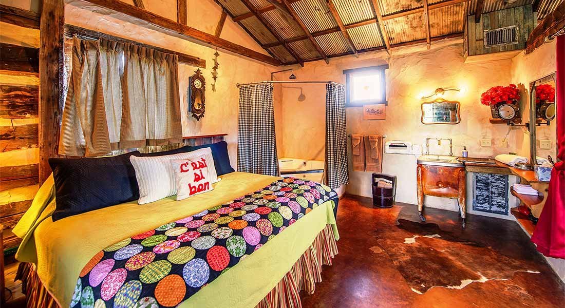A wide view of a rustic bedroom with a bed, window, sink, and mirror