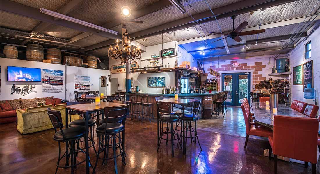 A dimly lit bar area with a chandelier, bar, seating area, tables, and chairs.