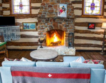 Sitting room with blue couch & marble-topped coffee table by fireplace in stone enclosure, kitchenette, table with seating for 2 along wall.