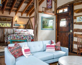 Living rooms with blue couch & ottoman, marble-topped coffee table. Table with chairs under window, bedroom with wrought iron furniture with floral comforter.