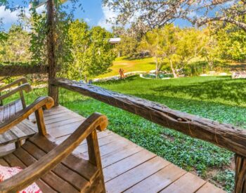 An inviting pair of wood rocking chairs on a wood deck looking out onto a green grass and tree filled yard.