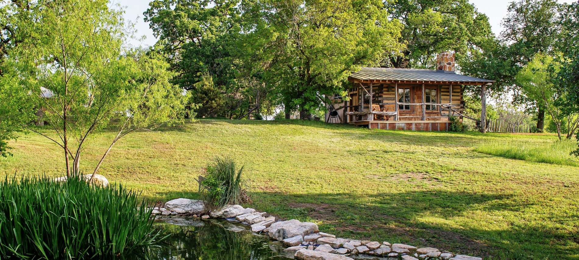 A log cabin with a porch and a pond in the foreground.