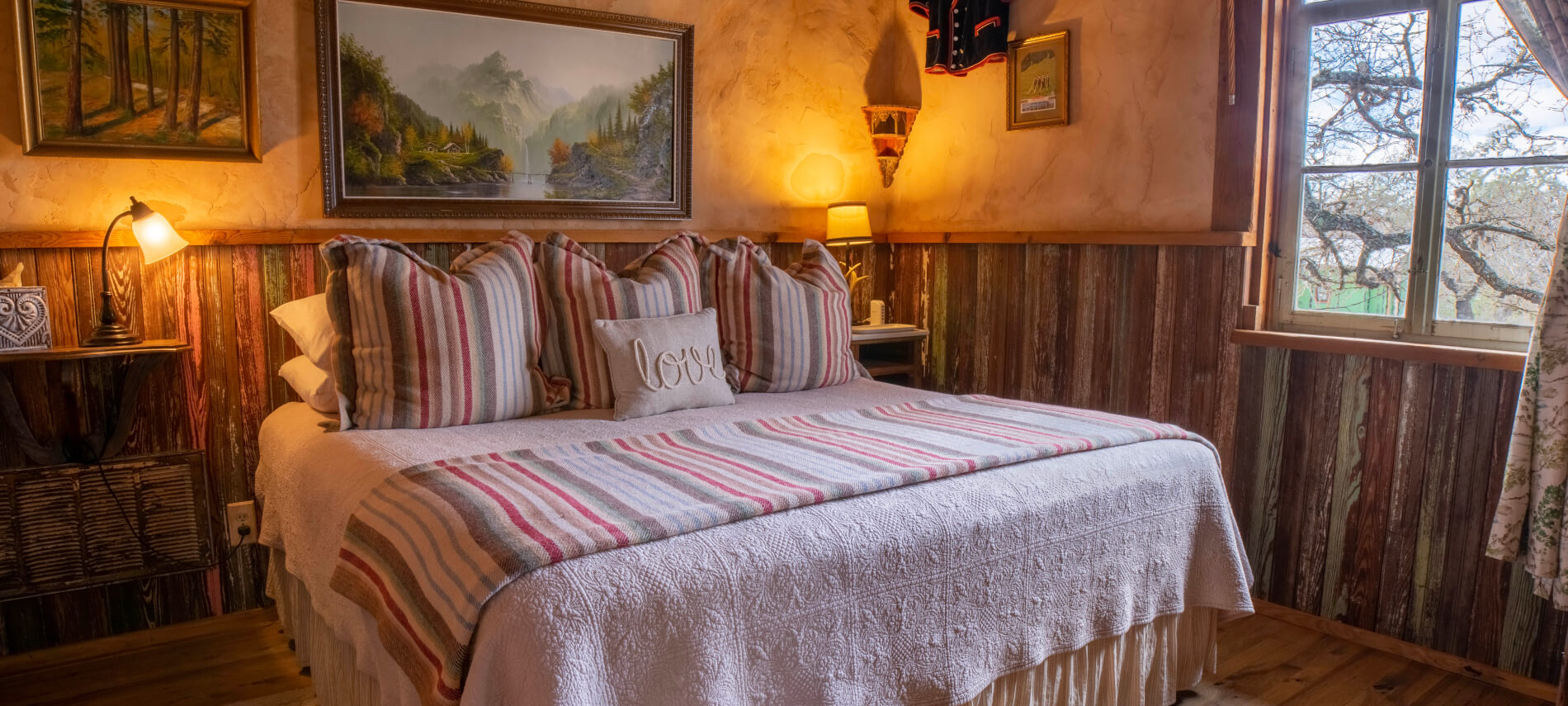 A bed with striped bedding and pillows, a painting on the wall, and a lamp on a nightstand.