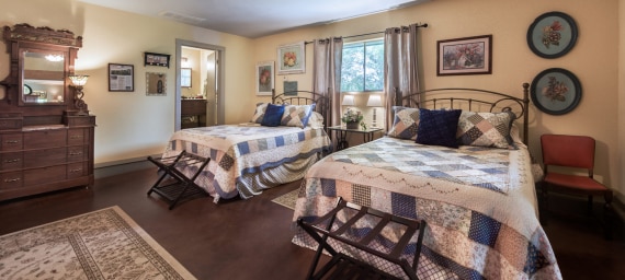 A wide view of a guest room with two beds, a dresser, and a window.