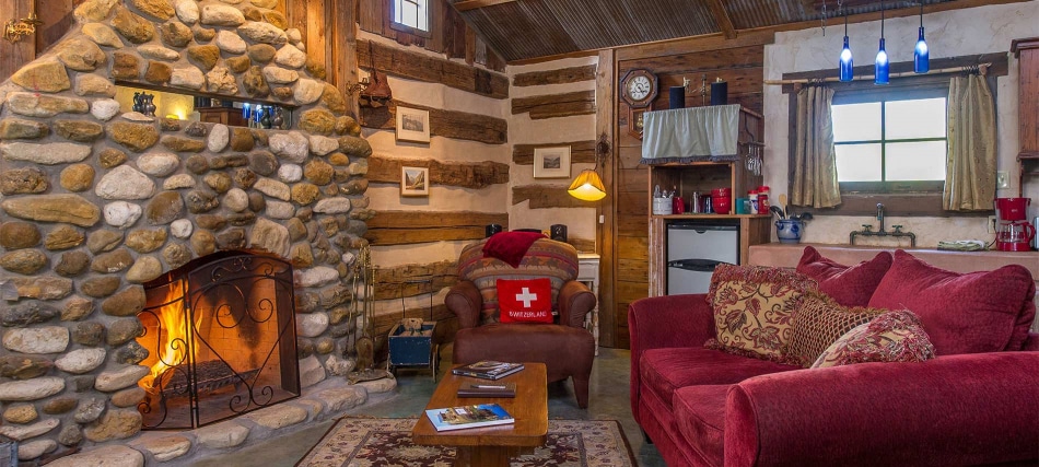 A cozy living room with a stone fireplace, log walls, and a red couch.