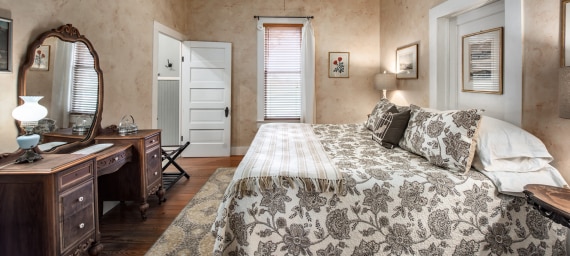 A wide view of a bedroom with a large bed, a wooden desk, and a mirror.