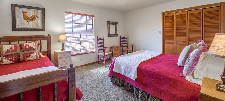 A wide view of a guest room with two beds, nightstands, a closet, and a window.