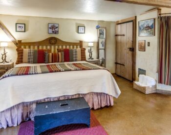 A country style bedroom with rustic walls with wood trim, a bed with Americana bedding, and a tub and shower on one wall.