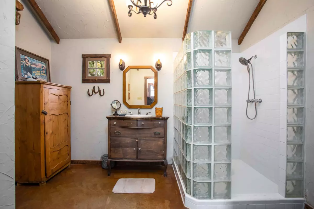 A bathroom with a glass block wall, wooden vanity, mirror, and shower.