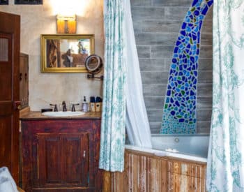 Inset bathtub with wooden frame with blue curtains surrounding, separate room with sink in oak cabinetry with mirror hanging above, towels in basket on floor.