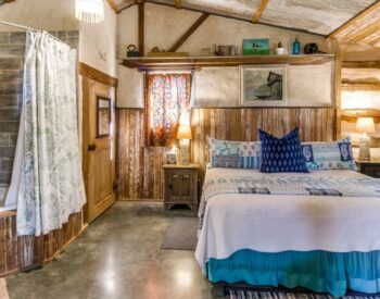 Country bedroom with wood walls and ceiling, a bed and a corner tub.