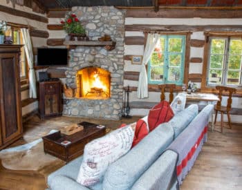 Long room with blue couch with pillows, tan chair on left, oak hutch, burning fireplace in stone enclosure.