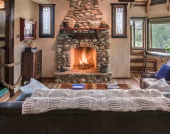 Brown leather couch facing burning stone-enclosed fireplace, wooden walls, Flat television on wall in separate room on left